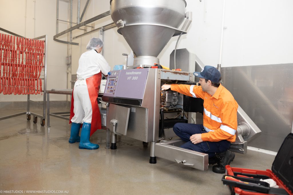 A VACPAC technician working on a machine while a factory worker works.