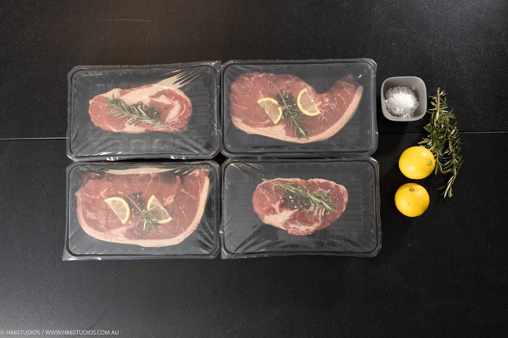 Four raw steaks vacuum sealed in individual pouches with lemon and rosemary